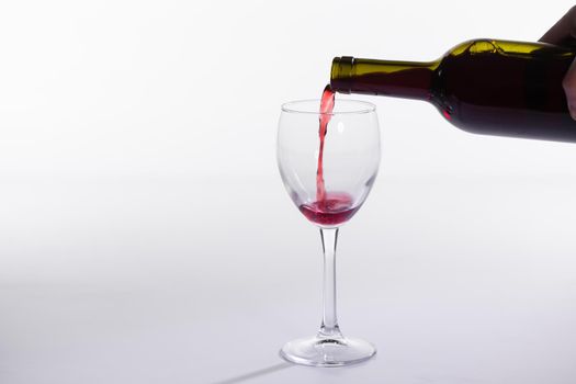 Pouring red wine into the glass on white background.