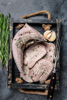 Cooked Boiled veal or beef tongue sliced in a wooden tray. Black background. Top view.