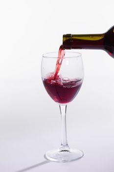 Pouring red wine into the glass on white background.