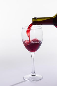 Red wine pouring into glass from bottle on white background.