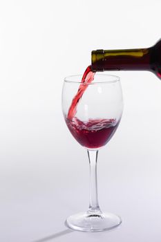 Pouring red wine into the glass on white background.