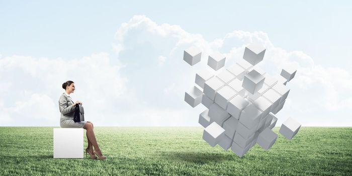 Elegant businesswoman with suitcase in hand sitting on white cube