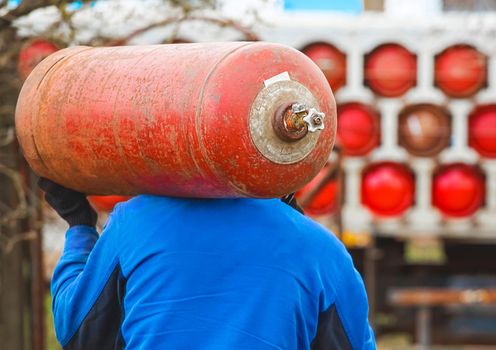 A male industrial worker walks with a gas cylinder to a gas car. Transportation and installation of a propane bottle to residential buildings.