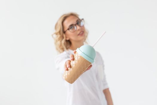 Cute charming young woman is holding a cocktail from a straw posing against a white background