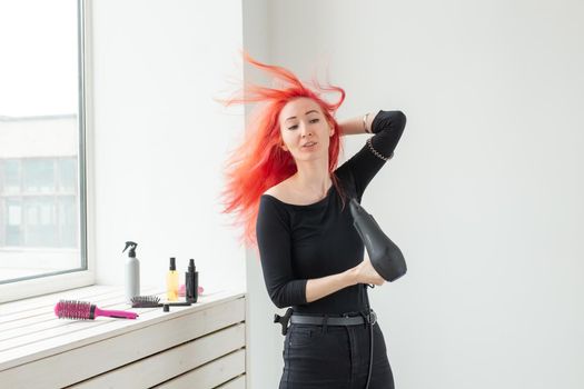 Hairdresser, beauty salon and people concept - young woman hair stylist with hair dryer on white background.