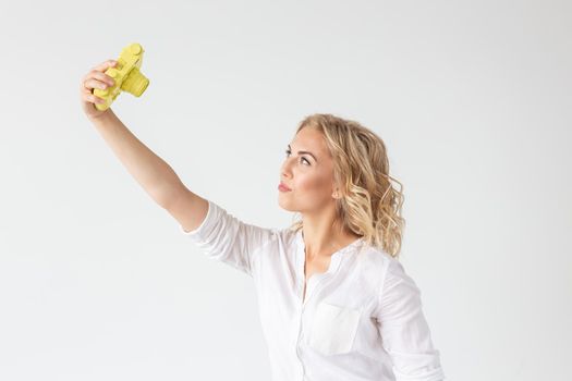 Smiling young woman is holding in her hands a yellow vintage camera model posing on a white background. Concept of amateur and professional photography