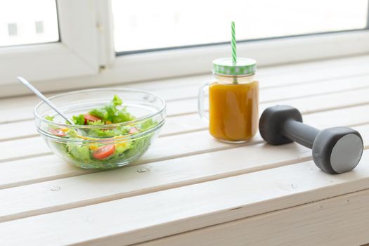 Vegetable salad fruit smoothies and dumbbell lie on a white windowsill. Concept of healthy lifestyle physical activity and proper nutrition