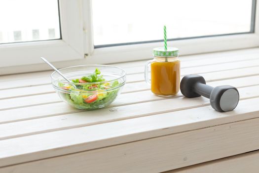 Vegetable salad fruit smoothies and dumbbell lie on a white windowsill. Concept of healthy lifestyle physical activity and proper nutrition