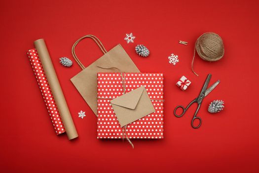 Close up packing and wrapping Christmas gifts with red and brown paper, table top view, flat lay