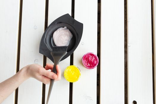 Color and hairdresser concept - female hairdresser in process of mixing hair dye color on the table with white background.