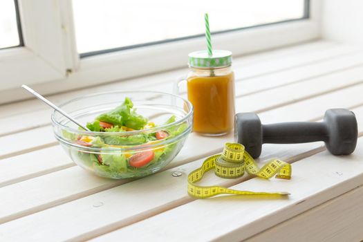 Vegetable salad fruit smoothies and dumbbell lie on a white windowsill. Concept of healthy lifestyle physical activity and proper nutrition