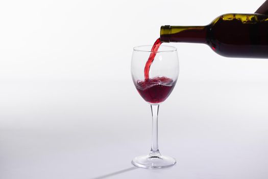 Red wine pouring into glass from bottle on white background.