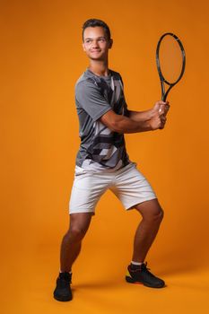 Full-length portrait of a tennis player man in action against orange background close up