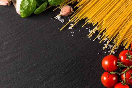 Food frame photo. Pasta ingredients. Cherry-tomatoes, spaghetti pasta, garlic, basil, salt  on dark grunge backdrop, copy space, top view, horizontal