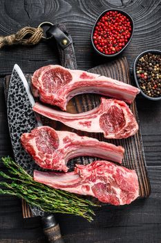 Lamb chops raw meat on bone with salt, pepper and herbs. Black wooden background. Top view.