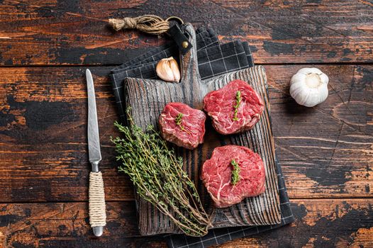 Prime raw Fillet mignon steaks on a wooden board with thyme and garlic. Dark wooden background. Top view.