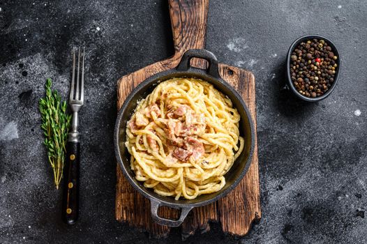 Pasta Carbonara with bacon and parmesan in a pan. Black background. top view.