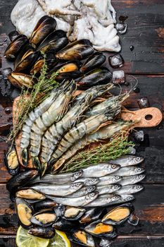 Assorted set of fresh seafood tiger prawns, shrimps, blue mussels, octopuses, sardines, smelt. Dark woodden background. Top view.