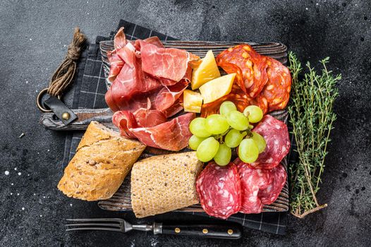 Cold meat plate, charcuterie - traditional Spanish tapas on a wooden board with bread and grape. Black background. Top view.