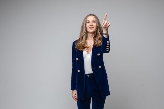 caucasian woman with attractive appearance points something her finger up, picture isolated on grey background