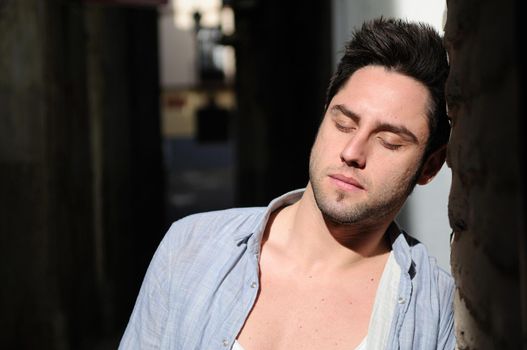 Portrait of young handsome man in urban background with eyes closed