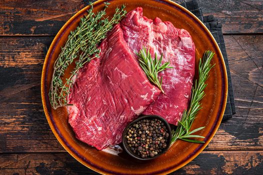 Two Flap or Flank raw beef steaks on a rustic plate with herbs. Dark wooden background. Top view.