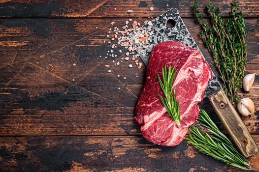 Raw Chuck eye roll Black Angus prime beef steak on butcher cleaver. Dark wooden background. Top view. Copy space.