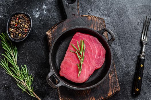 Fresh Raw tuna steak with rosemary in a pan. Black background. Top view.