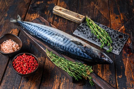 Fresh Raw fish Mackerel on a wooden cutting board with a cleaver. Dark wooden background. Top view.