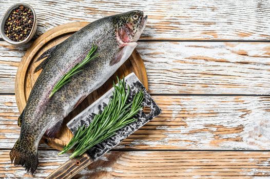 Rainbow trout on an wood board, with rosemary and cleaver. White wooden background. Top view. Copy space.