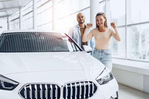 Young happy couple choosing a new car in car dealership