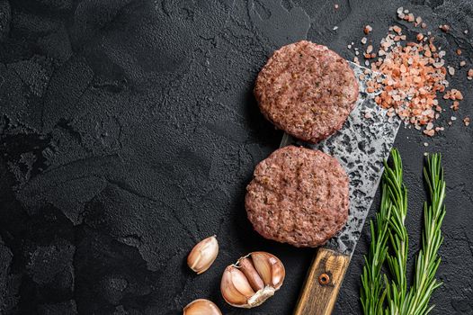 Butcher beef meat steak patties on a cleaver. Black background. Top view. Copy space.