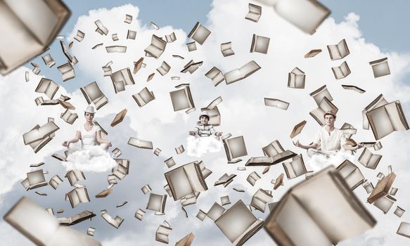 Young family keeping eyes closed and looking concentrated while meditating among flying books in the air with cloudy skyscape on background.