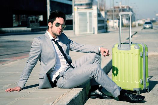 Man dressed in suit and suitcase sitting on the floor in the street