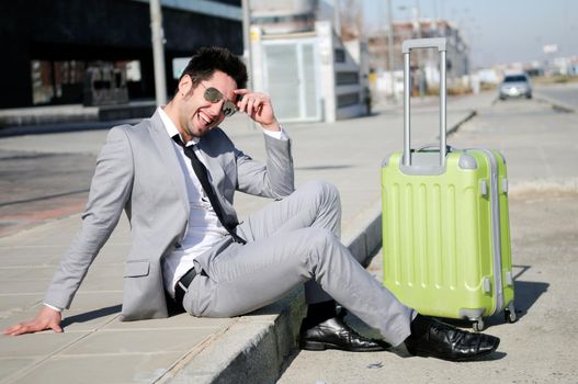 Man dressed in suit and suitcase sitting on the floor in the street