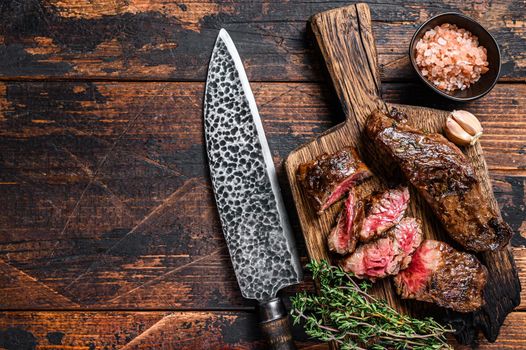 Grilled bbq skirt steaks slices on a wooden board. Dark wooden background. Top view. Copy space.