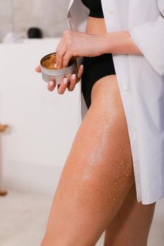 Woman applying nourishing scrub on body on bathroom background, closeup. Spa at home concept