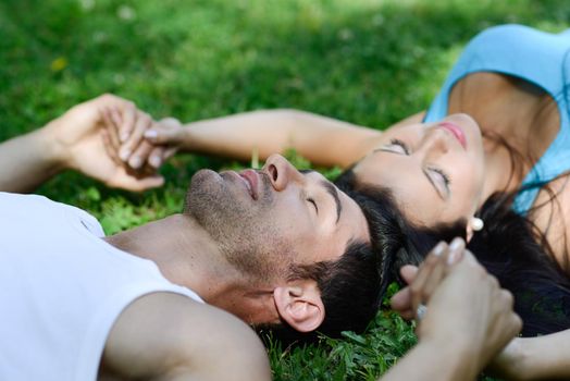 Happy smiling couple laying on green grass in a beautiful park