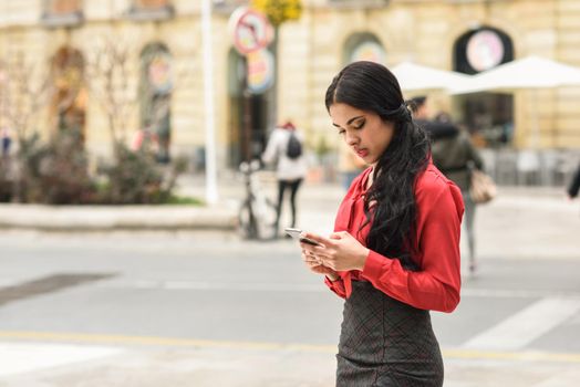 Portrait of hispanic businesswoman in urban background looking at her mobile phone