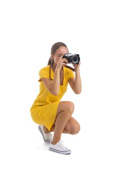 Young caucasian woman in yellow dress takes images with photo camera. Full length portrait. Isolated on the white background.