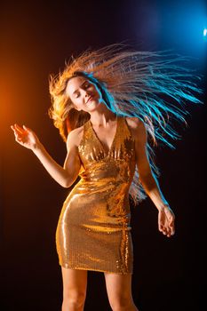 Beautiful girl in Golden dress dancing on black background in night club, color lights