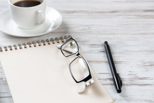Top view office desk with white cup of coffee. Flat lay vintage wooden table with spiral notebook, glasses and pen. Coffee break time. Corporate business concept. Relax at work with hot drink.
