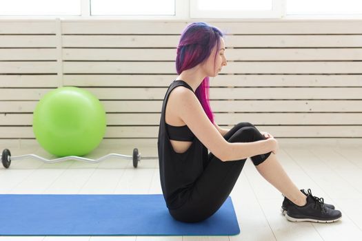 Young slim girl with colored hair makes an headstand on a sports blue mattress next to a barbell and green fitball. Concept of good physical fitness and regular training in the gym