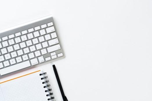 Top view of modern working place. Spiral notepad, pen and computer keyboard on white surface. Education, creativity and innovation concept with copy space. Digital technology in modern business.