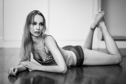 Beautiful blonde woman in white lingerie laying on wooden floor. Young girl wearing underwear with long hair. Female wearing t-shirt and red panties.