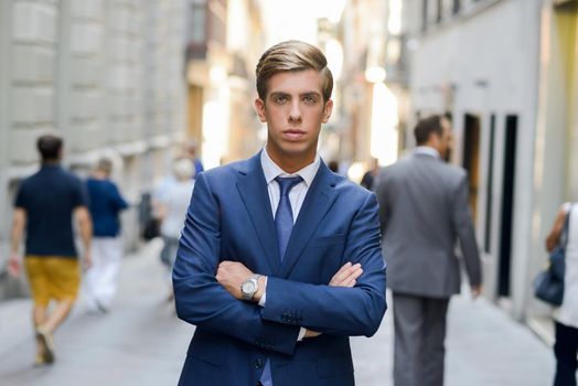 Portrait of an attractive young businessman in urban background wearing blue suit a necktie. Blonde hair
