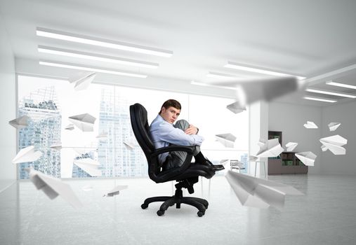 scared businessman sitting on a chair with his hands clasped his knees. paper plane is flying around