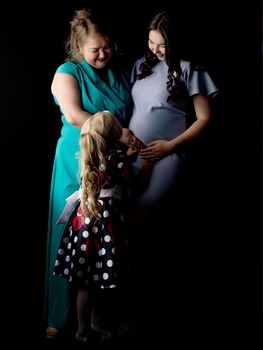 Young pregnant girl with her mother and younger sister on a black background.