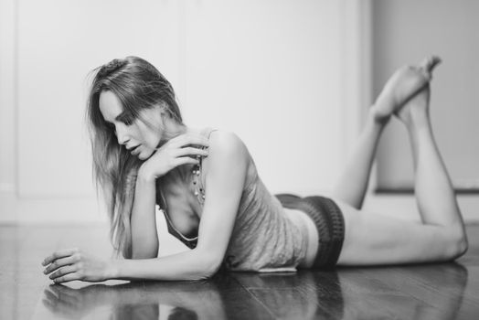 Beautiful blonde woman in white lingerie laying on wooden floor. Young girl wearing underwear with long hair. Female wearing t-shirt and red panties.
