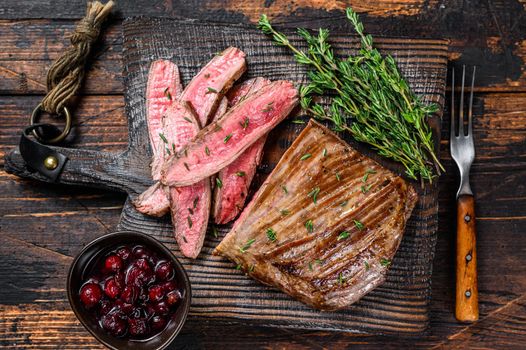 Barbecue sliced flank beef meat steak on a wooden cutting board. Dark wooden background. Top view.